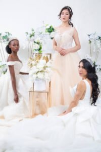 Three women in wedding gowns styled together with white floral arrangements in a studio setting