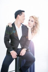 Pre wedding photoshoot makeup sydney: couple in a studio portrait, the woman with blonde curled hair leaning on the man's shoulder