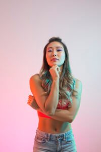 Woman in a red bralette and jeans posed under pink and teal gel lighting in a studio