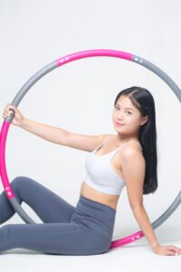 Woman in athletic wear holding a pink and grey hula hoop against a white studio background